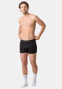 Czarne bokserki z elastycznym paskiem z logo, zestawione z białymi sportowymi skarpetami. Materiał wydaje się gładki, a fason dopasowany.