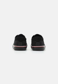 Baskets noires avec une texture lisse, un design minimaliste, présentant une bande blanche et rouge sur la semelle intermédiaire et un talon rembourré.