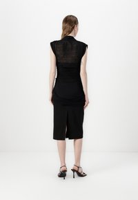 Zwarte jurk met korte mouwen, gerimpelde details en een middellange rok met een zijsplit. Semi-doorschijnende stoffen achterkant en een gladde textuur.