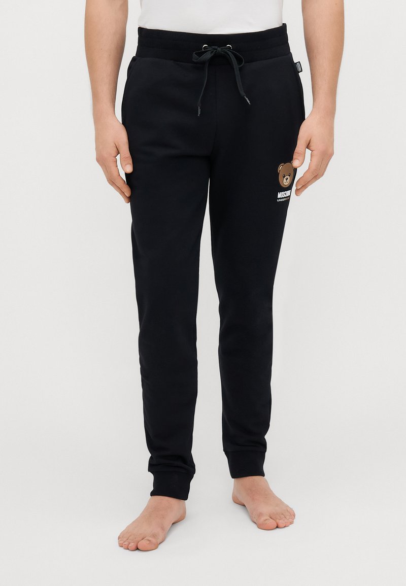 Mornarske pamučne trenirke s elastičnom trakom u struku, sužavajući se prema dnu, s grafikom medvjeda na lijevom bedru. Mekana tekstura i elastični manšeti.