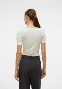 Witte geribde T-shirt met korte mouwen en een vierkante halslijn, gecombineerd met donkergrijze taps toelopende broeken met achterzakken.