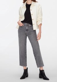 Chaqueta blanca de botones, camisa negra debajo, jeans grises de tiro alto, corte recto y recortado, llevados con botas negras hasta el tobillo.