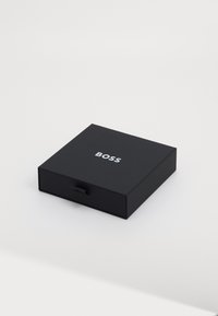 Svart, rektangulær boks med skuffer, med en hvit "BOSS"-logo på toppen. Glatt, matt tekstur. Ingen ekstra mønstre eller detaljer.