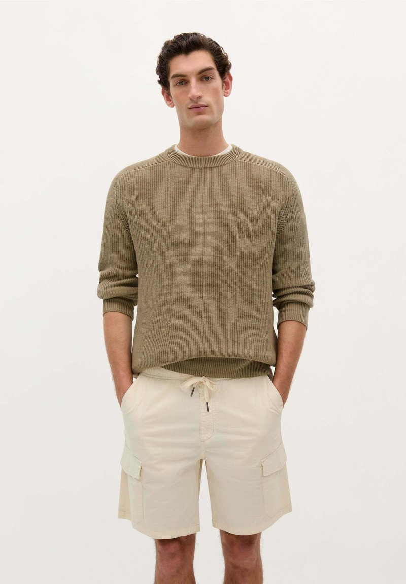 Pull en maille vert olive avec texture côtelée, associé à un short cargo beige avec poches latérales et ceinture élastique.