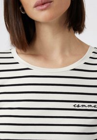 Gestreiftes Hemd aus weißer und schwarzer Baumwolle mit rundem Halsausschnitt und kleinem gesticktem 'Komma'-Logo auf der unteren rechten Seite.