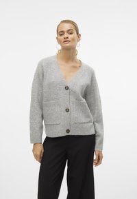 Cardigan en laine gris avec un col en V, trois boutons et deux poches avant. Ourlet et poignets côtelés, avec une finition douce et texturée.