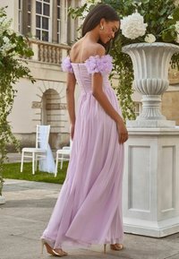 Rochie lila deschis, cu umerii goi, cu mâneci din tul plisate, bust cu pliu și fustă fluidă, completată cu pantofi cu toc metallic.