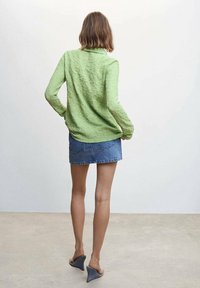 Chemise verte texturée à manches longues associée à une jupe en denim clair. La tenue est complétée par des chaussures compensées grises.