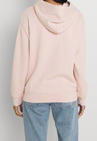 Ljusrosa hoodie med en avslappnad passform, stor huva och ribbade manschetter. Matchad med ljusblå jeans med en urtvättad look och standardfickdesign.