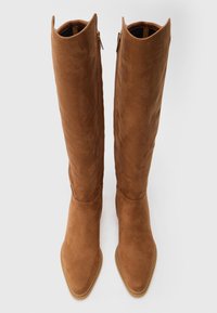 Bottes en daim marron jusqu'au genou avec un bout pointu, une texture lisse et des fermetures éclair sur les côtés. Design épuré avec un détail de semelle cousue subtil.