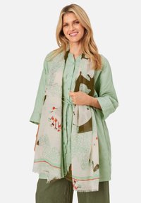 Light green linen shirt with a button front, paired with a patterned scarf featuring organic shapes in green, white, and orange accents.
