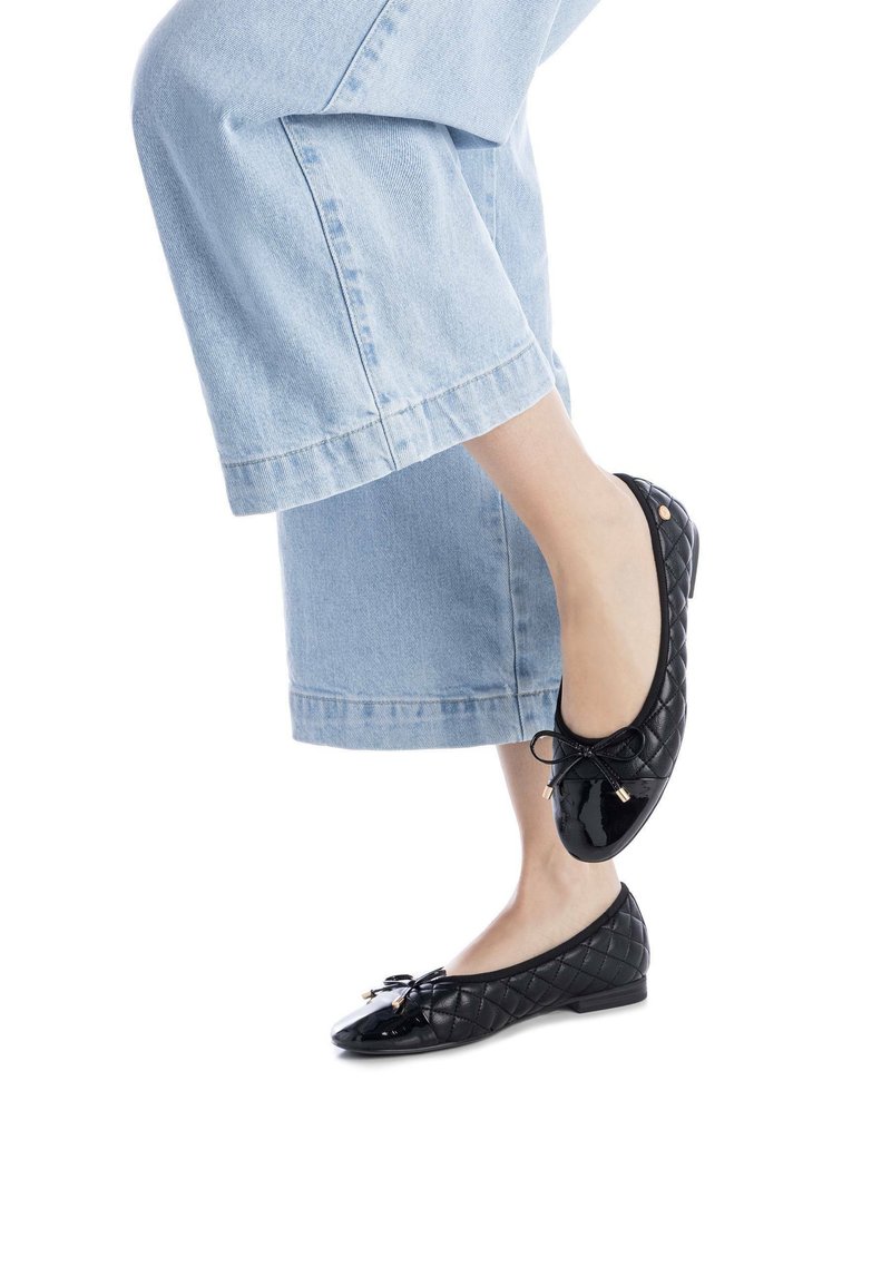 Bailarinas de charol negro con acolchado, que presentan una pequeña decoración de lazo y detalles en dorado, combinadas con unos vaqueros de pierna ancha de color azul claro.