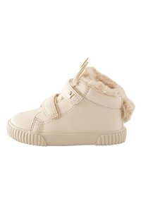 Cream faux leather shoe with a plush fur trim, featuring two Velcro straps and a textured rubber sole. Rounded toe with a slightly raised back.