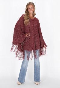 Cardigan en tricot bourgogne avec franges, à coupe ample, motif texturé et cinq boutons sur le devant. Associé à un jean évasé bleu clair.
