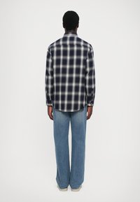 Marine rutete flanellskjorte med hvite ruter, lange ermer, knappede mansjetter og buet kant, kombinert med lys blå vide jeans.