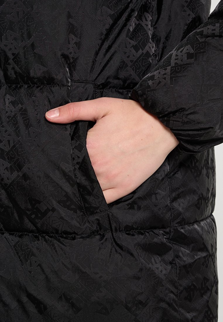 Schwarze Daunenjacke mit einem subtilen geometrischen Muster, mit einer Hand in einer Seitentasche, die die glatte, glänzende Textur und das warme Design zur Schau stellt.