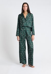 Zelený pyžamový set vyrobený z lehkého materiálu, s potiskem jelenů na pozadí lesa, s klopovým límcem a elastickým pasem.