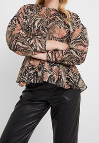 Blouse à manches longues et col rond en tissu transparent à motifs aux tons terreux de brun, orange et noir. Ourlet volanté et épaules froncées.