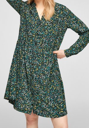 Robe imprimée florale avec une base noire, présentant des fleurs vertes, jaunes et blanches. Manches longues, décolleté en V et une silhouette fluide en A.