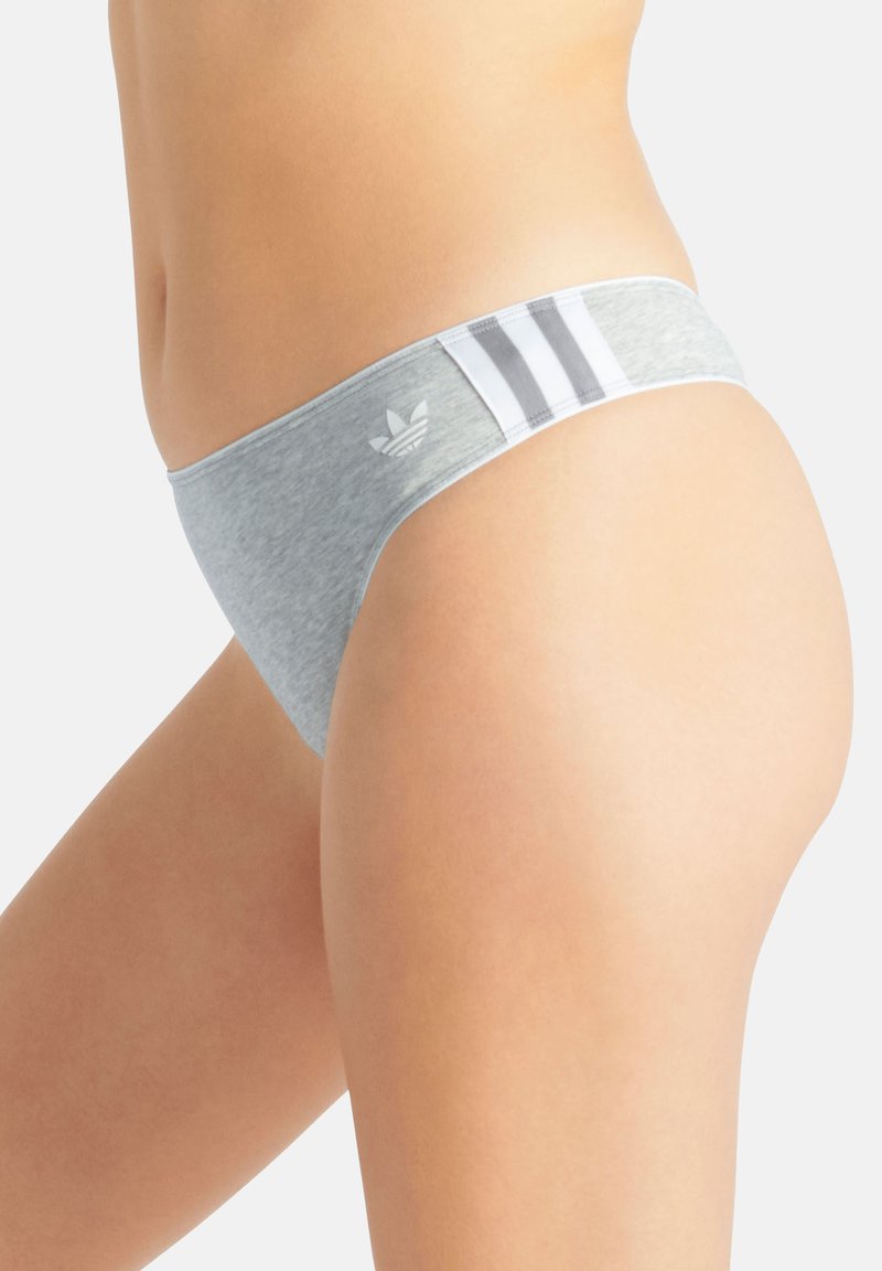 Primo piano di una persona che indossa slip bikini grigi Adidas con strisce bianche e logo sulla cintura.