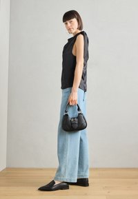 Top sin mangas de satén negro, jeans de pierna ancha azul claro, zapatos planos negros y un bolso negro pequeño con detalles en plata.