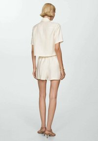 Cream-colored short-sleeve cropped shirt and matching shorts in lightweight fabric. Smooth texture, relaxed fit, subtle stitching details.