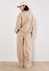 Conjunto de sudadera y pantalones beige en tejido suave, con un corte relajado, puños acanalados y un diseño simple. Combinado con una gorra a juego.