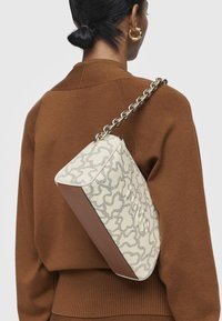Bolso beige con patrón abstracto plateado, forma rectangular, acentos marrones y una asa de cadena metálica gruesa. Detalle de superficie texturizada.