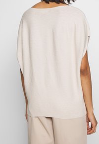 Beige överdimensionerad stickad topp med vid halsringning, korta dolmansärmar och mjukt tyg. Har en lös passform och rundad nederkant.