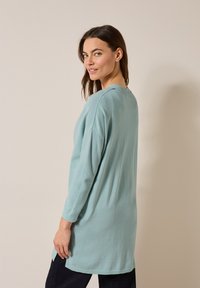 Ljusblå, långärmad tröja i ett mjukt, strukturerat tyg med avslappnad passform och sidoöppningar, i kombination med mörka byxor.