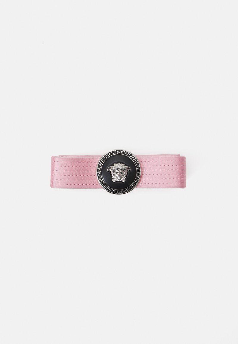 Pink satin belt featuring a circular black medallion with a lion head design and a decorative silver trim, highlighting intricate details.