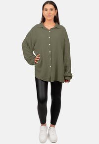 Olijfgroene, loszittende button-up shirt gemaakt van textiel; gecombineerd met zwarte legging en witte sneakers.