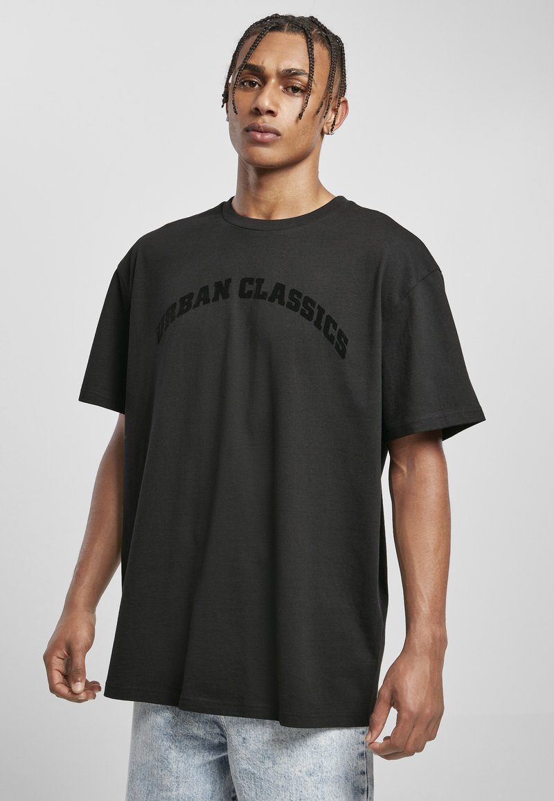 T-shirt en coton noir à manches courtes avec un col rond, arborant "URBAN CLASSICS" en lettres majuscules en relief sur la poitrine.