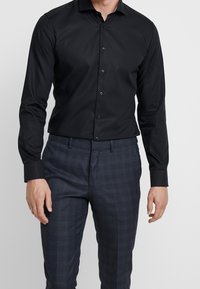 Czarna koszula na długi rękaw z guzikami, o dopasowanym kroju i gładkiej strukturze, zestawiona z granatowo-czarnymi spodniami w kratę.