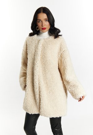 Palton oversized de culoare crem, realizat dintr-un material texturat și pufos, cu mâneci lungi și croială dreaptă, asortat cu pantaloni negri din piele.