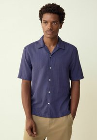 Short-sleeve, button-front shirt in textured dark navy fabric. Features a camp collar and a straight hem with two front buttons.