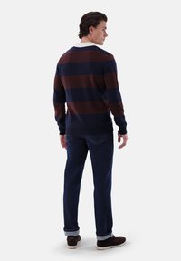 Gestreifter Pullover aus Wolle mit horizontalen Navy- und Bordeaux-Rottönen, ausgestattet mit einem weißen Kragen. Kombiniert mit dunklen Jeans und braunen Wildlederschuhen.