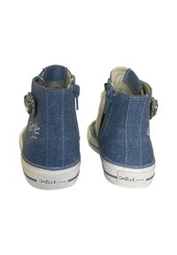 Sneakers alte in denim con chiusura a zip, di colore blu, suola in gomma bianca e accento decorativo in gemma sul lato.