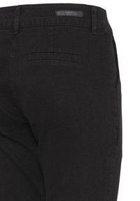 Mustad musta slim-fit püksid, millel on nähtav tagatasku ja vöökoht, millel on väike must brändi silt valgel taustal.