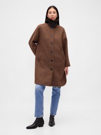 Cămașă cu un model în carouri maro, cu guler înalt, închidere cu butoane în față și buzunare laterale. Purtați peste blugi albaștri și cizme negre până la gleznă.