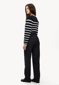 Pull cropped à rayures noires et blanches avec des manches longues, associé à un pantalon noir ajusté et des mocassins noirs. Texture lisse, style décontracté.