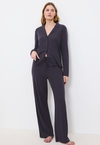 Tweedelige pyjama-set in donkergrijs. Bevat een knoopsluiting, lange mouwen top met kraag en bijpassende joggingbroek met een relaxte pasvorm.