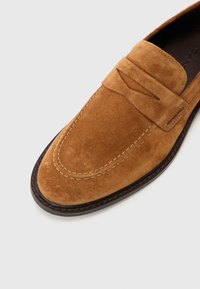 Vaaleanruskeat mokkanahka loaferit, joissa on pehmeä pinta ja mokkasiinityylinen kärki. Varustettu ommelluilla yksityiskohdilla ja tummanruskealla kumipohjalla.