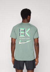 Πράσινο αθλητικό μπλουζάκι με κοντά μανίκια, που διαθέτει μεγάλο γραφικό σχέδιο στην πλάτη με κείμενο και το λογότυπο της Nike σε αντίθετους χρωματισμούς.