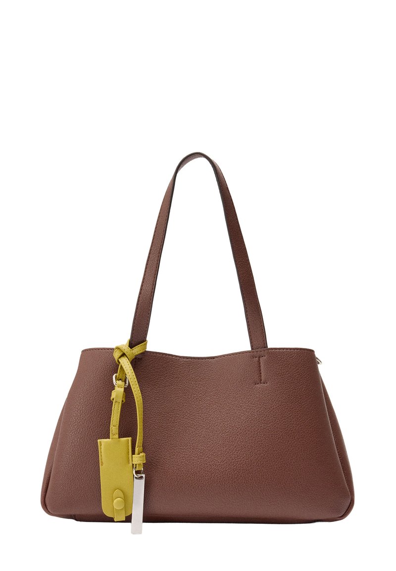 Brązowa skórzana torebka na podwójnych ramiączkach, z żółtą metką i srebrnym metalowym akcentem zawieszonym na jednym z ramiączek.