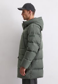 Roheline puhvjakken, millel on kapuuts, tikandiga osad, ees pikk tõmblukk ja kangas allservas. Kantakse tumeda pesapallimütsiga.