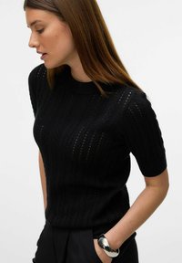 Černý pletený top s krátkým rukávem s texturovaným vzorem a žebrovaným výstřihem. Nosit s černými kalhotami s vysokým pasem a stříbrným náramkem.