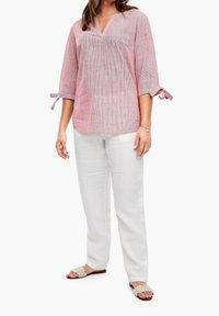 Blouse légère à rayures rouges et blanches avec un décolleté en V, des manches trois-quarts et des détails noués aux poignets, associée à un pantalon en lin blanc.