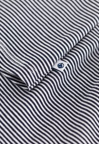 Gestreepte stof in marineblauw en wit, met horizontale lijnen. Een klein label met een logo is zichtbaar in de onderste hoek. Zachte textuur.