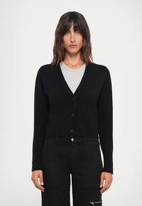 Svart kort cardigan med v-hals, lange ermer og fem-knappers lukking. Laget av et mykt materiale med ribbestrikket kant og glatt tekstur.